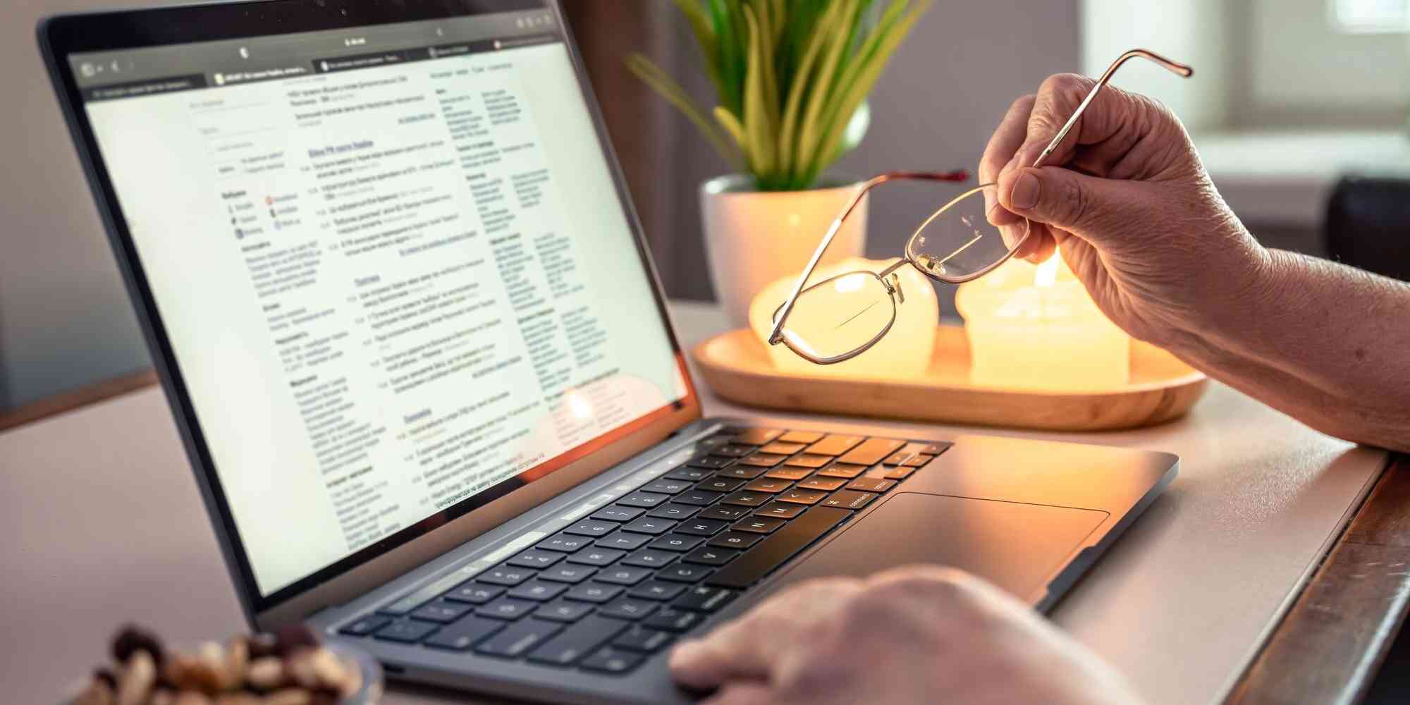 图中是一名男子手持着眼镜，正在使用笔记本电脑，电脑屏幕显示的是文件内容。